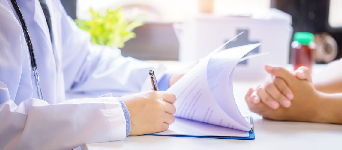 Doctor man consulting patient while filling up an application form at the desk in hospital. Medicine and health care concept