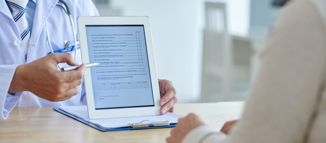 Close-up shot of physician pointing at screen of digital tablet, female patient listening to him with concentration